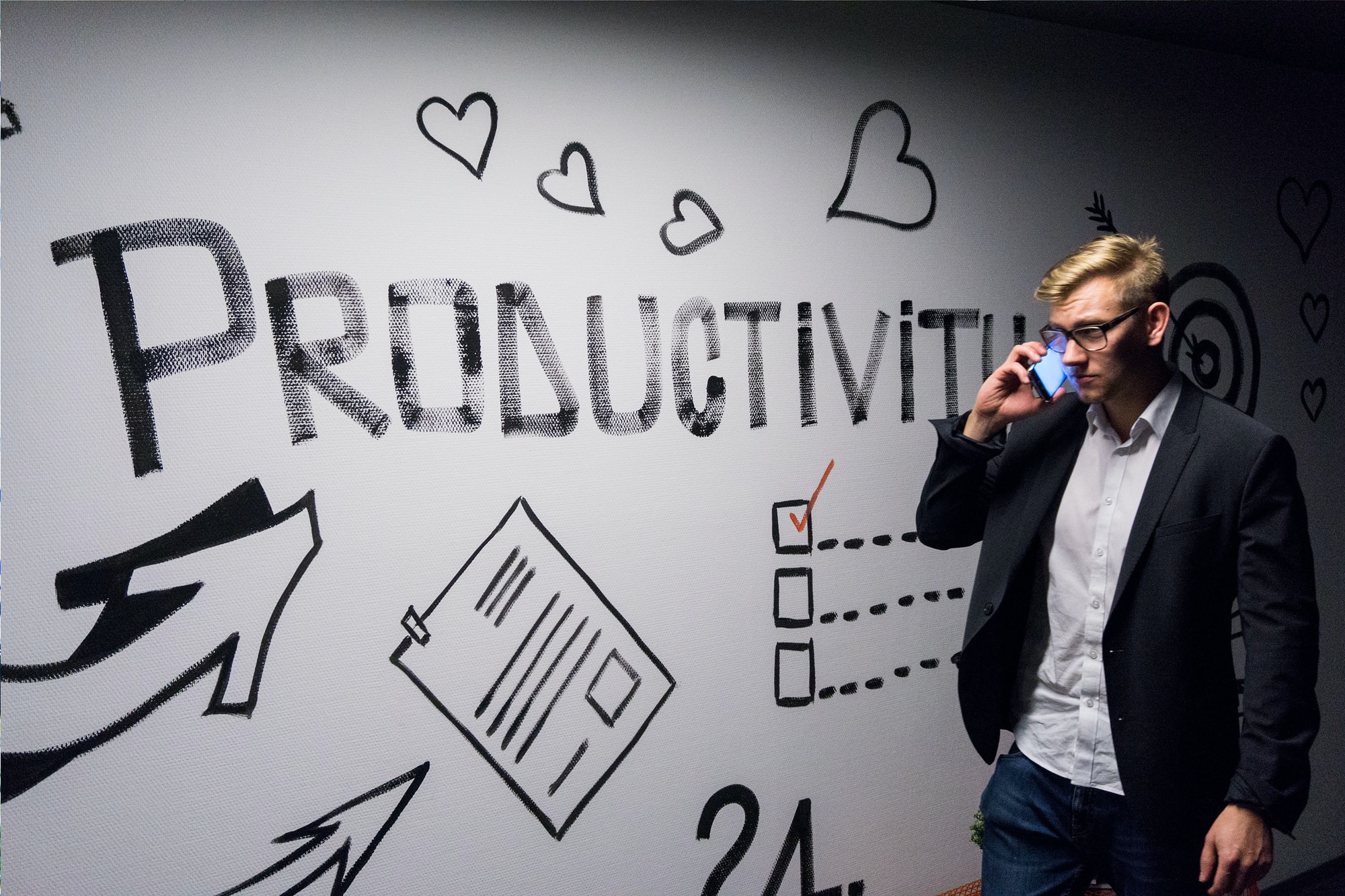 Picture of man in suit drinking something standing in front of a whiteboard with the word "productivity" written on it. 